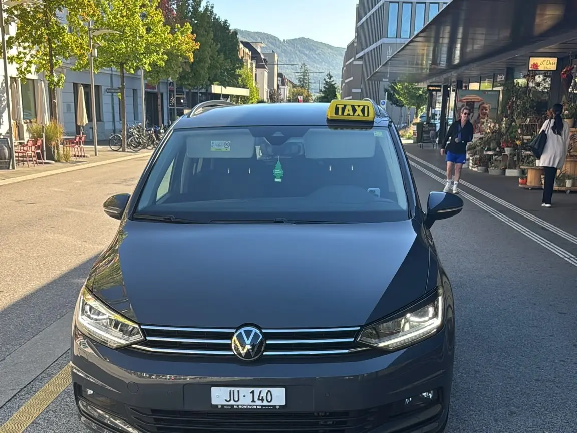 Taxi d'Andrea VW Touran JU 140 dans une rue de Delémont, avec les crêtes du Jura en arrière-plan